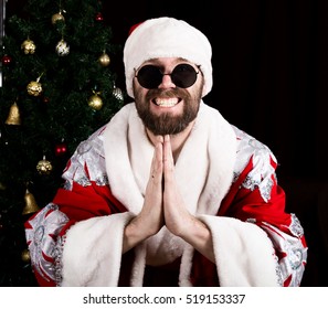 Bad Rastoman Santa Claus Smiles And Making Hands Sign Namaste On The Background Of Christmas Tree