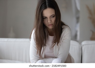 Bad streak. Sad suffering nervous millennial woman sitting on couch with her head down, looking aside feeling stress depression guilt shame, having health problems, unable to make difficult decision