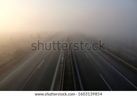 Bad weahter photography. High angle view of driving on a gray foggy day on the highway. Low visibility condition. Difficult and dangerous hazard for drivers. Drive safely in autumn and in winter.