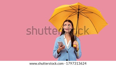 Bad Weather Concept. Portrait of unhappy lady holding smart phone and umbrella at studio, looking confused, banner