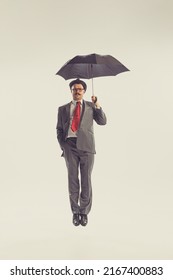 Bad Weather. Portrait Of Young Man Dressed In 50s, 60s Style Fights The Wind With Umbrella Isolated On White Background. Autumn Fashion Collection. Concept Of Culture, Art, Wellbeing, Beauty And Ad.