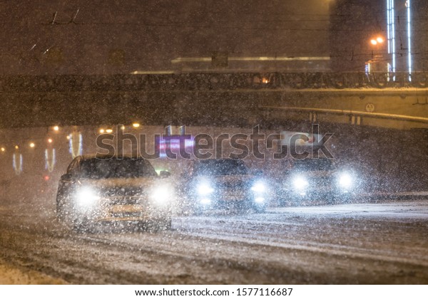 Bad\
winter weather and poor visibility. Cars driving on the roadway\
during a snowstorm/blizzard at night. Soft focus.\
