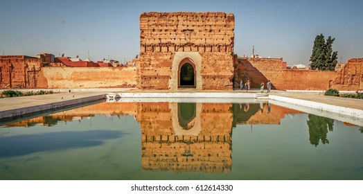 Badi Palace in Marrakech with reflection in water pond in front and tourists in the background