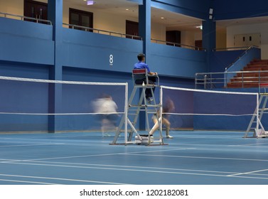 A Badminton Court Number 8 In Action Seeing Movements Of Double Female Players Playing While Focusing On An Umpire On Duty In The Mid Court.