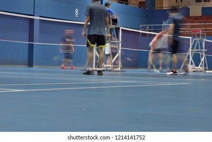 A Badminton Court Number 8 In Action Seeing Movements Of Double Female Players Playing While Focusing On An Umpire On Duty In The Mid Court.