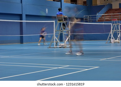 A Badminton Court Number 8 In Action Seeing Movements Of Double Female Players Playing While Focusing On An Umpire On Duty In The Mid Court.