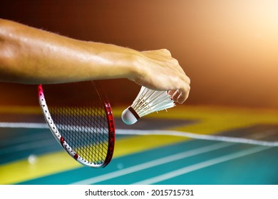 Badminton player is holding white badminton shuttlecock and badminton racket in front of the net before serving it over the net to another side of badminton court. Selective focus on white shuttlecock