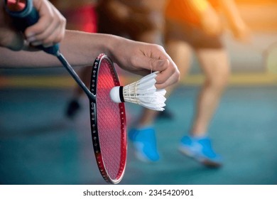 Badminton player is holding white badminton shuttlecock and badminton racket in front of the net before serving it over the net to another side of badminton court. Selective focus on white shuttlecock