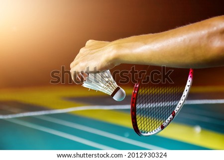 Badminton player is holding white badminton shuttlecock and badminton racket in front of the net before serving it over the net to another side of court. 