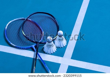 Badminton rackets and white cream badminton shuttlecocks after playing or after games on blue floor of indoor badminton court, soft focus, concept for badminton lovers around the world.