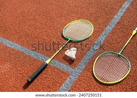 Badminton shuttlecocks and racket, placed in the corner of a synthetic field.