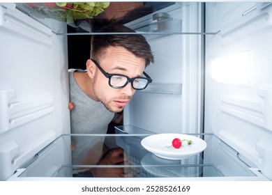 Baffled Man Looking Inside an Almost Empty Fridge