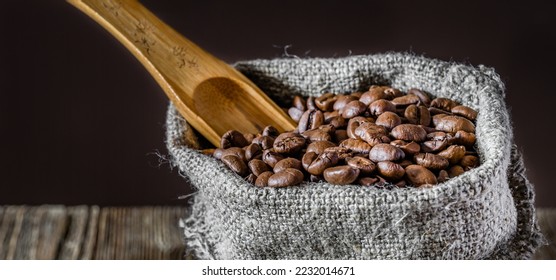 A bag of coarse canvas of coffee beans and wooden spoon. Coffee beans scattered on the wooden tabletop. Background with dark wood texture. Сlose-up - Shutterstock ID 2232014671