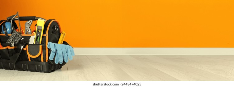 Bag with different tools for repair on floor near orange wall, space for text. Banner design