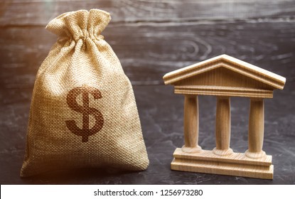 A Bag With Dollar Money And A Bank Or Government Building. Deposits, Investment In The Budget. Grants And Subsidies. Payment Of Taxes. Central Bank. Credit Tranches And Leases. Debt Repayment.