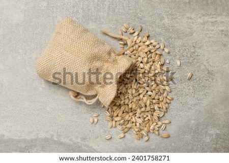 Bag with dry pearl barley on gray table, top view