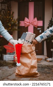 Bag Of Gifts At Christmas Under The Door. Delivery Of New Year's Gifts. Santa Claus Bag With Congratulations. Xmas Porch Decor, Kraft Paper Bag With Christmas Boxes In Hand