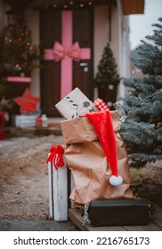 Bag Of Gifts At Christmas Under The Door. Delivery Of New Year's Gifts. Santa Claus Bag With Congratulations. Xmas Porch Decor, Kraft Paper Bag With Christmas Boxes