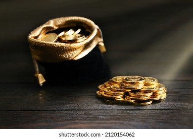 A bag with gold coins on a wooden background. The money in a black bag on a wooden table. Treasure Hunt. A Purse with money. Wallet wit gold coins