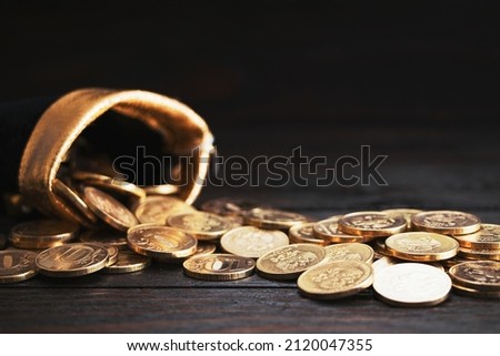 A bag with gold coins on a wooden background. The money is in a black bag. Treasure Hunt.Copy space. Place for text