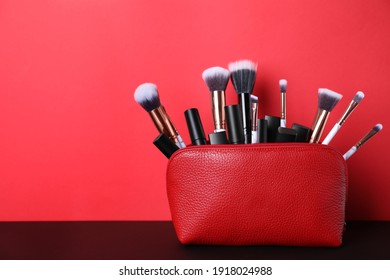 Bag With Makeup Brushes And Cosmetic Products On Black Table Against Red Background. Space For Text