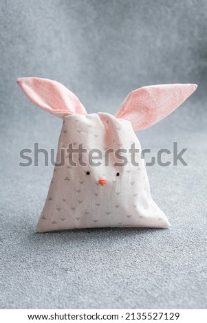 Bag of sweets in shape of Easter bunny with ears on light gray background. Packing made of cotton fabric in form of cute bunny or rabbit, sewing for children, hobby. Vertical Easter card, copy space.