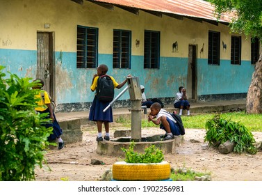 BAGAMOYO, TANZANIA - JANUARY 2020: Young Girls in Tanzanian School Uniform Are Pumping water and Drinking fron the Water Pump in Yard. Garden getting fresh water in the community. Hand water pump in