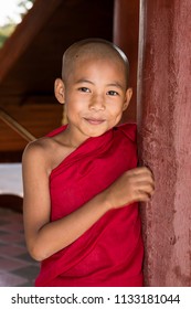 Bagan, Myanmar, December 29, 2017:  Young Buddhist novice looks mischievously behind a red pillar in a pagoda in Bagan, Myanmar