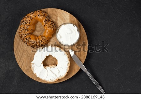 Bagel and cream cheese as a concept for breakfast. Wooden tray, black background, top view, copy space.