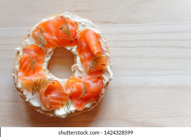 a bagel with cream cheese, cured salmon(lox,gravlox) and dill, top view, wood background