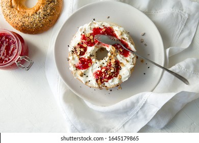 Bagel With Cream Cheese And Raspberry Jam On A White Plate