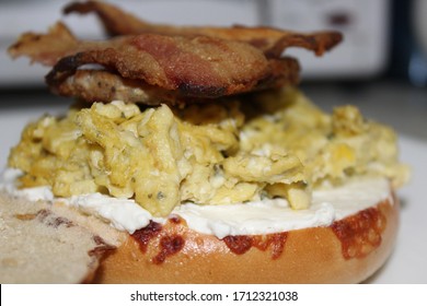 A Bagel With Pesto Scrambled Eggs And Bacon On Top