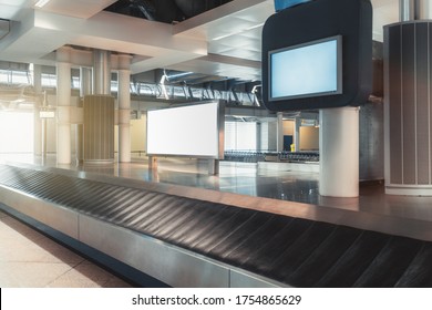 A Baggage Claim Area In A Hall Of A Modern Airport Arrival Zone With Conveyor Belt And A Mock-up Of White Empty Advertising Or Information Billboard On A Chrome Surface, Bluish Tv Plasma Screen Above