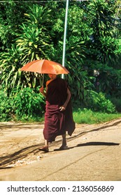Bago , Myanmar - December 02 2012 : a buddhist monk with robe on and umbrella to protect against the sun is walking on a Bago Myanmar village dirt road