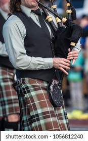 Bagpipe player mouthpiece and hands making music in traditional Irish kilt.