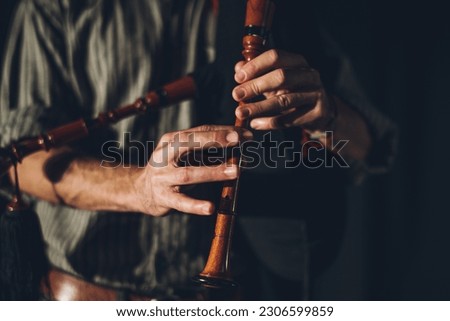 Bagpipe player playing his instrument in an auditorium with stage lights and a black background.