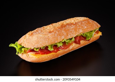 Baguette Sandwich With Ham, Smoked Sausage, Cheese, And Green Salad On A Black Background.