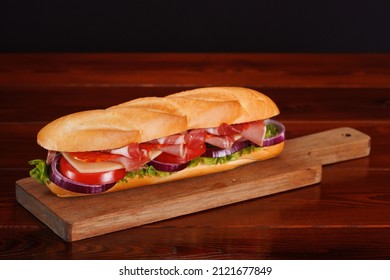 Baguette Sandwich With Ham, Smoked Sausage, Cheese, Tomato, Red Onion And Green Salad On A Wooden Table. Selective Focusing.