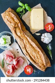 Baguette Sandwich Ingredients - Ham, Cheese, Butter, Tomatoes, Basil, Dark Stone Background, Top View