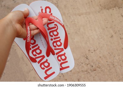 Bahia, Brazil - December 4, 2020: Woman Holding Brazilian Havaianas Flip Flops Sandals On Sandy Beach. 