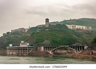 Baidicheng, China - May 7, 2010: Qutang Gorge on Yangtze River. Green vegetation on hill slopes with tower, high rise buildings, bow bridge and house on multi-level stilts on shoreline.