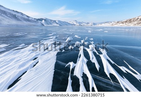 Baikal Lake in February cold day. Unusual winter landscape with white coastal mountains and iced bay. On the surface of blue ice snow crusts in form of frozen waves. Beautiful winter background
