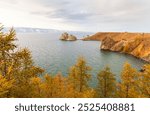 Baikal Lake on October. View of famous Shamanka Rock - natural landmark of Olkhon Island. Natural background. Bright autumn landscape with yellowed larch trees on coast. Autumn traves and outdoors