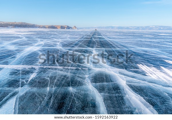 Baikal lake, Road trip, Travel concept, Road\
way on surface of the natural ice in frozen water behind the\
mountain island at Baikal lake, Russia,\
2019