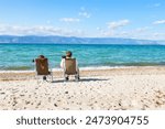 Baikal Lake in summer. Two tourists sit on sandy beach of Olkhon Island, look at the mountains through binoculars, take pictures of the Small Sea and enjoy outdoor recreation. Summer travel and rest