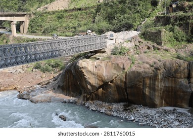 Bailey bridge spans a rugged mountain river in a high-altitude region, providing a strong and reliable crossing amid the dramatic Himalayan landscape.