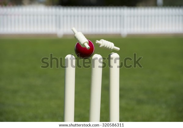Bails\
fly from cricket stumps as ball hits on grass\
field