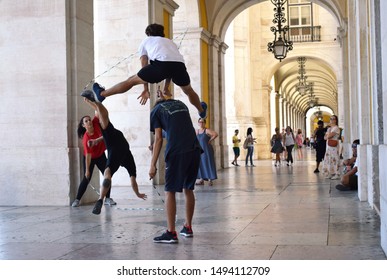 Baixa, Lisbon, Portugal. August 28 2019. Young People Practising Acrobatics Mixed With Double Dutch Skipping While Passers By Look On In Lisbon's Public Colonnade Walk Way Next To The Augusta Arch 