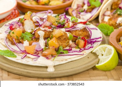 Baja Fish Tacos - Soft shell tacos filled with seasoned fried white fish served with red cabbage, pineapple salsa, chunky guacamole and creamy Baja style sauce.