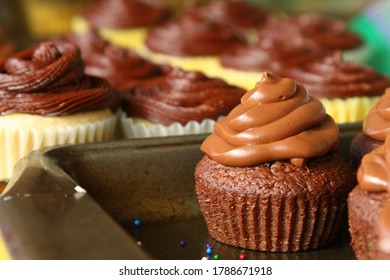 A Bake Sale Table With Homemade Chocolate Cupcakes With Rich, Swirled Chocolate Frosting Topping. More Cupcakes Are In The Background.